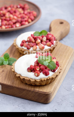 Wild strawberry tartlets with cream filling, delicious summer fruit mini tarts on rustic cutting board Stock Photo