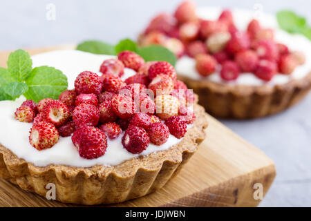 Wild strawberry tartlets with cream filling, delicious summer fruit mini tarts on rustic cutting board Stock Photo