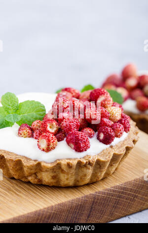 Wild strawberry tartlets with cream filling, delicious summer fruit mini tarts on rustic cutting board Stock Photo