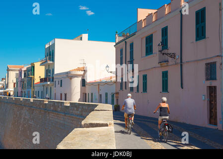 Mature couple cycling Mediterranean, a middle aged couple cycle alongside the old seawall in the harbor area of Alghero, Sardinia. Stock Photo