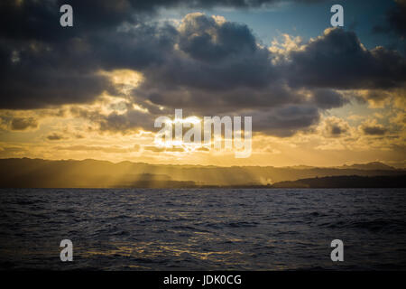 Yellow rays filter down through the clouds onto the mountains of an island in the Caribbean Stock Photo