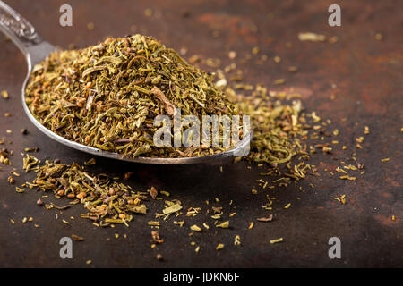 Spoon filled with dried thyme on rusty background Stock Photo