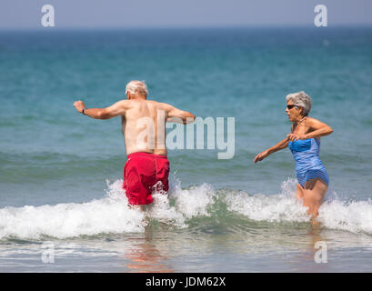Elderly couple man and woman splashing in the waves during a uk heatwave in June 2017 having fun at the popular seaside destination of Bedruthan Steps, Cornwall, England