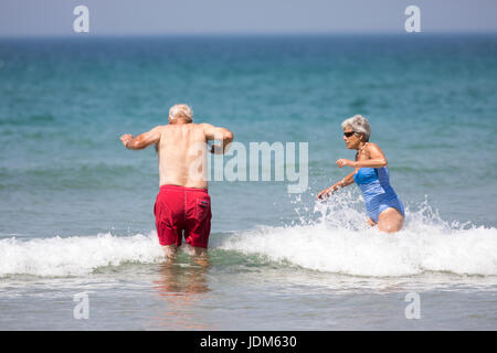 Elderly couple man and woman splashing in the waves during a uk heatwave in June 2017 having fun at the popular seaside destination of Bedruthan Steps, Cornwall, England