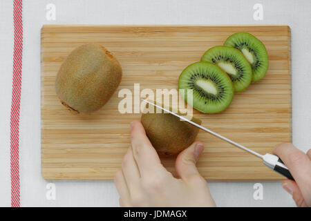 Hands slicing a kiwi on a wooden board Stock Photo