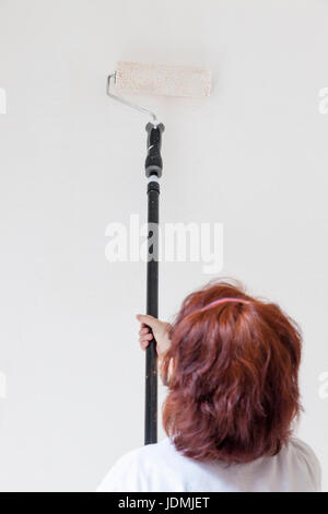 Woman painting a wall white using a paint roller Stock Photo