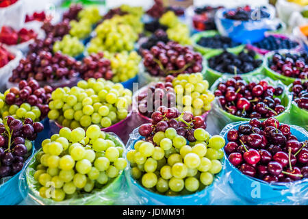 Closeup of many green and red grapes and cherries in baskets on display in market Stock Photo