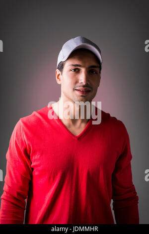 A young man with red wool sweater, wearing baseball cap, front view. On dark background Stock Photo