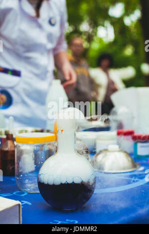 Various chemical utensils on the table. In front is a flask in which a chemical reaction Stock Photo