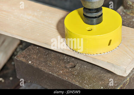 Drilling a large hole in the board with a core drill on a vertical drilling machine Stock Photo