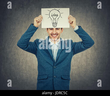 Smiling businessman or teacher holding a white paper above his head with a light bulb sketch. Science and business idea concept isolated on grey backg Stock Photo
