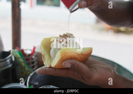Saler scooping coconut Ice-cream topped with peanut and milk dressing on bread.Traditional coconut ice-cream in Thailand Stock Photo