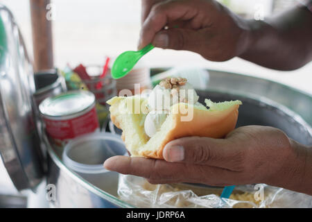 Saler scooping coconut Ice-cream topped with peanut and milk dressing on bread.Traditional coconut ice-cream in Thailand Stock Photo