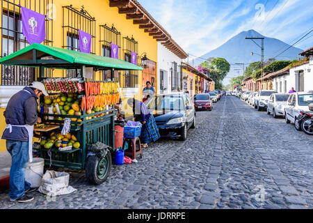 Antigua, Guatemala - April 2, 2017: Fruit seller, colorful houses & Agua volcano in colonial city & UNESCO World Heritage Site of Antigua during Lent Stock Photo