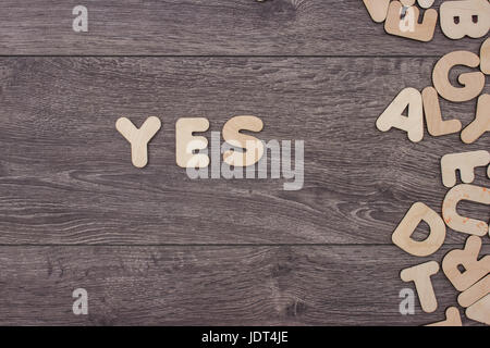 Word Yes made with wooden letters next to a pile of other letters over the wooden board surface composition Stock Photo