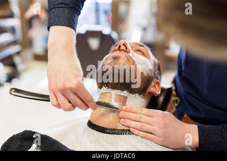 man and barber with straight razor shaving beard Stock Photo
