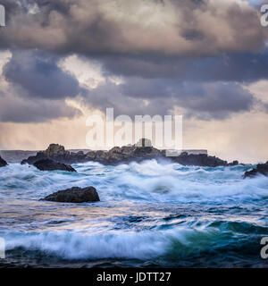 Stormy ominous sky and sea with waves breaking on rocky shore of Irish coast Stock Photo