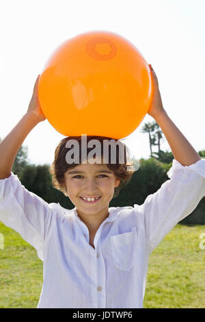 Young kid holds an orange ball over head Stock Photo