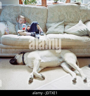 Little girl on couch next to big dog Stock Photo