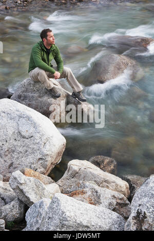 Mid adult man sitting on rocks in river Stock Photo