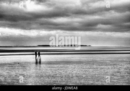 Couple walking out to Hilbre Island Stock Photo