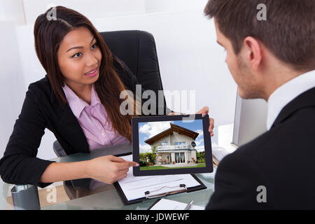 Businesswoman showing digital tablet to male colleague with house photo Stock Photo