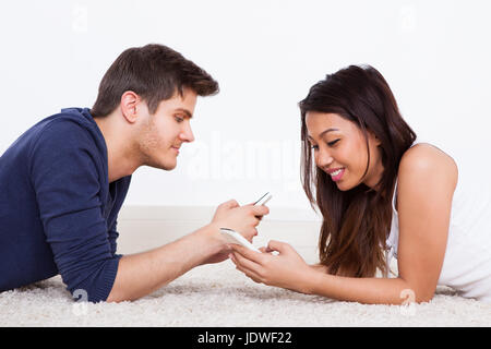 Side view of young couple using cellphones while lying on rug at home Stock Photo