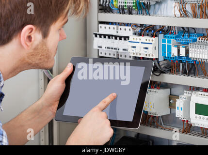 Side view of male technician examining fusebox while holding tablet Stock Photo