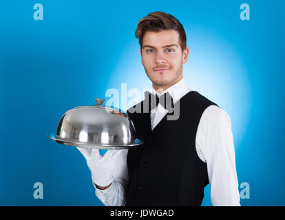 Portrait of confident butler carrying tray over blue background Stock Photo