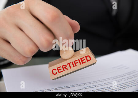 Closeup of hand stamping document with Certified rubber stamp at table in office Stock Photo