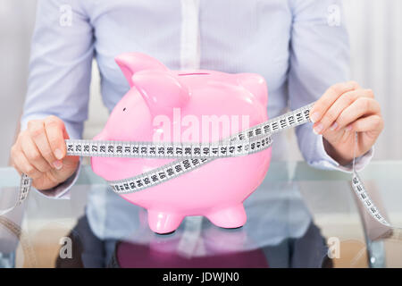 Close-up Of Businessperson Holding Measuring Tape Around An Pink Piggybank Stock Photo