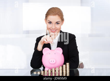 Portrait Of Happy Young Businesswoman Inserting Coin In Piggybank Stock Photo
