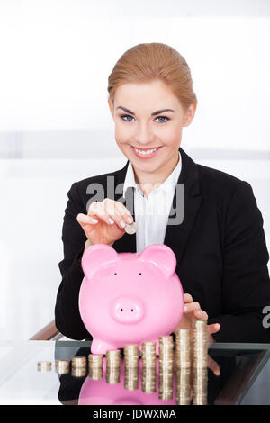 Portrait Of Happy Young Businesswoman Inserting Coin In Piggybank Stock Photo