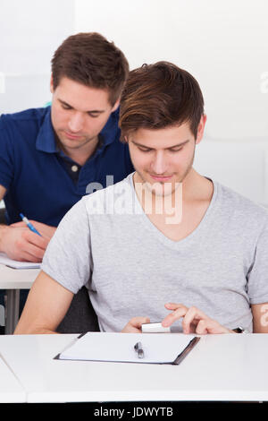 Young male university student using mobile phone at desk in classroom Stock Photo
