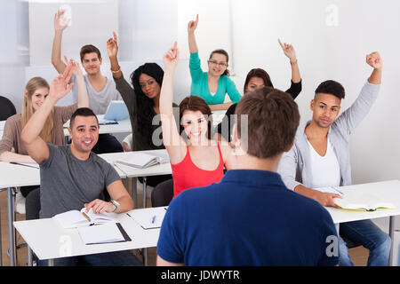 Group of university students with hands raised answering teacher in classroom Stock Photo