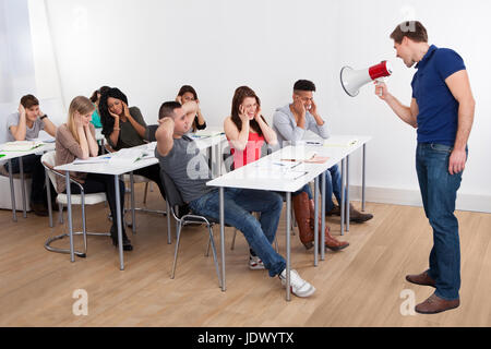 Angry teacher shouting through megaphone on university students in classroom Stock Photo