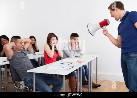 Angry teacher shouting through megaphone on university students in classroom Stock Photo