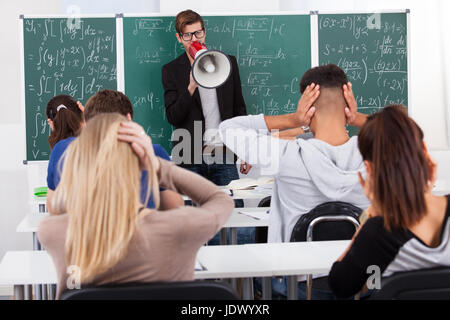 Young teacher shouting through megaphone on university students in classroom Stock Photo