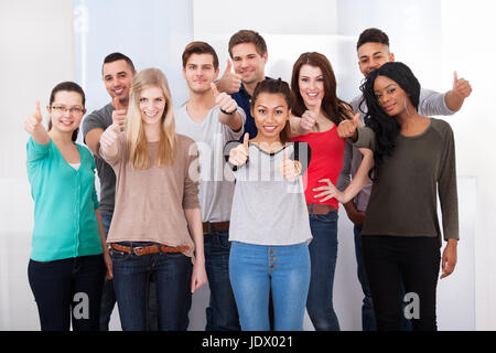 Group portrait of confident multiethnic college students gesturing thumbs up in classroom Stock Photo