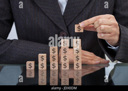 Midsection of businesswoman stacking dollar blocks at desk Stock Photo
