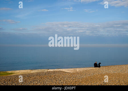 Man and dog sitting on empty beach, Hove, UK Stock Photo