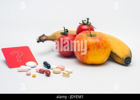 verschiedene bunte Tabletten, Apfel, Banane, Tomaten und rotes Fragezeichen-Schild, isoliert