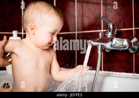 Cute baby playing with water tap in bathroom Stock Photo