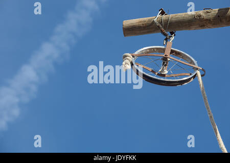 Wheel rim made of a baby trolley with rope over blue sky. It used for the renovation of the facade of the building Stock Photo