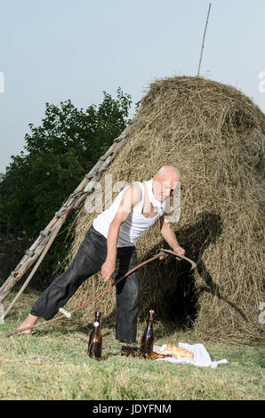 Senior farmer using scythe to mow the lawn traditionally. Stock Photo
