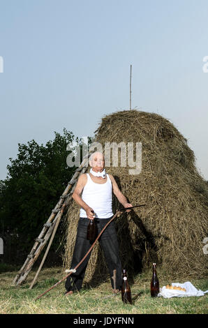 Senior farmer using scythe to mow the lawn traditionally. Stock Photo