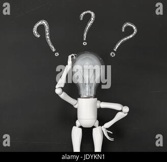 a standing lamp character scratches his bulb light switched off with his right hand and has three white questions marks drawn by chalk around his head on the blackboard behind him Stock Photo