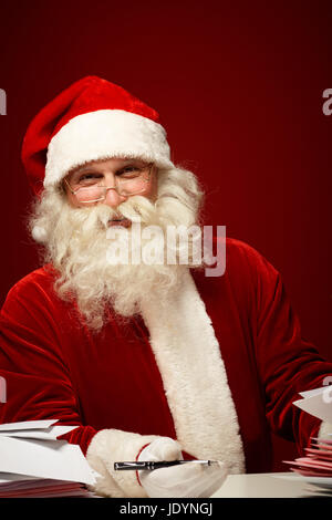 Smiling Santa Claus with pen looking at camera while answering Christmas letters Stock Photo