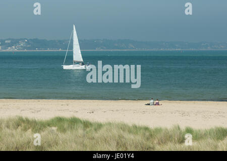 Studland Beach, Purbeck Peninsular, Dorset, UK, 21st June 2017. On what might be that last day of the current heatwave, it’s a hot and sunny day on the beautiful sandy stretch of the south coast popular with holidaymakers and day trippers alike. A sea breeze and temperature of 24 degrees. A white sail yacht sailing by. Stock Photo