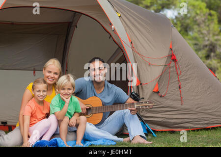 Portrait of happy family at the campsite in front of tent with father holding guitar Stock Photo